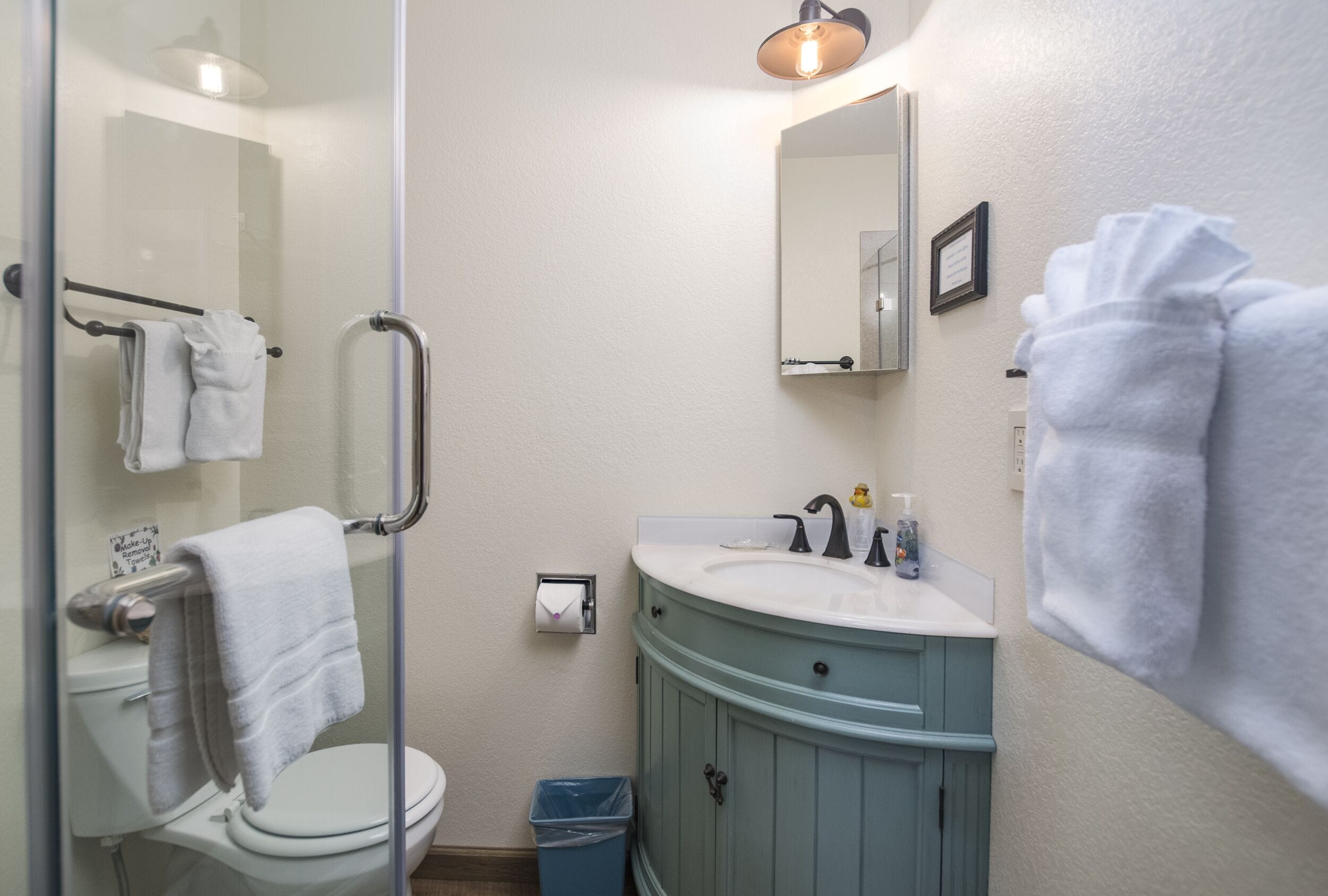 A bathroom with a glass shower enclosure, a white toilet, a blue vanity with a sink, and a mirror above the sink.