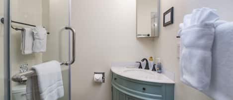 A bathroom with a glass shower enclosure, a white toilet, a blue vanity with a sink, and a mirror above the sink.