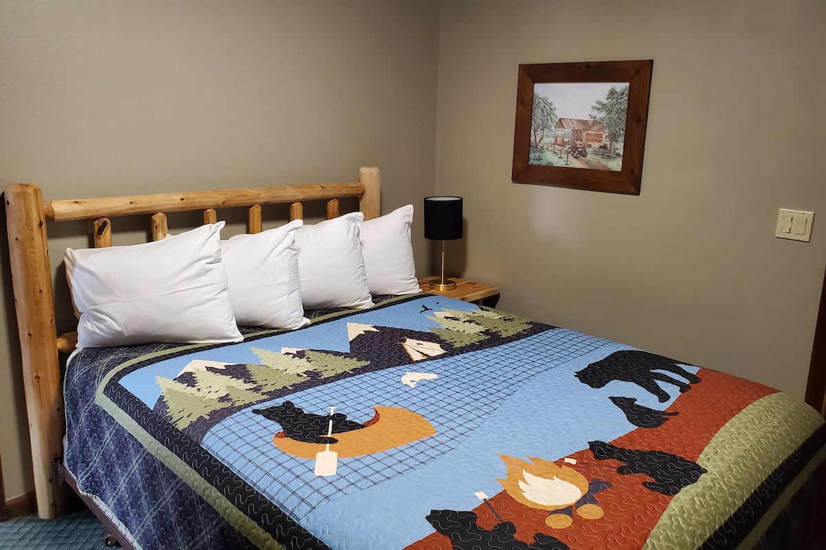 Ein Bett mit Holz-Kopfbrett, weißen Kissen und einer Decke mit einer Naturdarstellung.