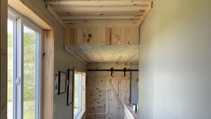 Un corridoio stretto con pareti e soffitto in legno, ampie finestre su un lato e, sul lato opposto, un angolo cottura con un bancone e pensili.