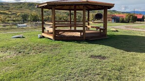 Un gazebo in legno con tetto in metallo, immerso in un prato e con un paesaggio collinare sullo sfondo.