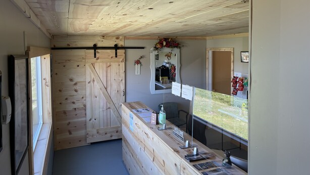 Ambiente interno in legno con una porta scorrevole, un banco reception e vista sull'esterno.