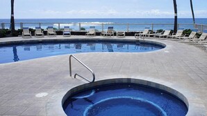 A swimming pool with a small hot tub, lounge chairs, and a view of the ocean.