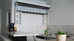 Une cuisine moderne avec des meubles blancs, une machine à café, un évier et une plante en pot posée sur le plan de travail.