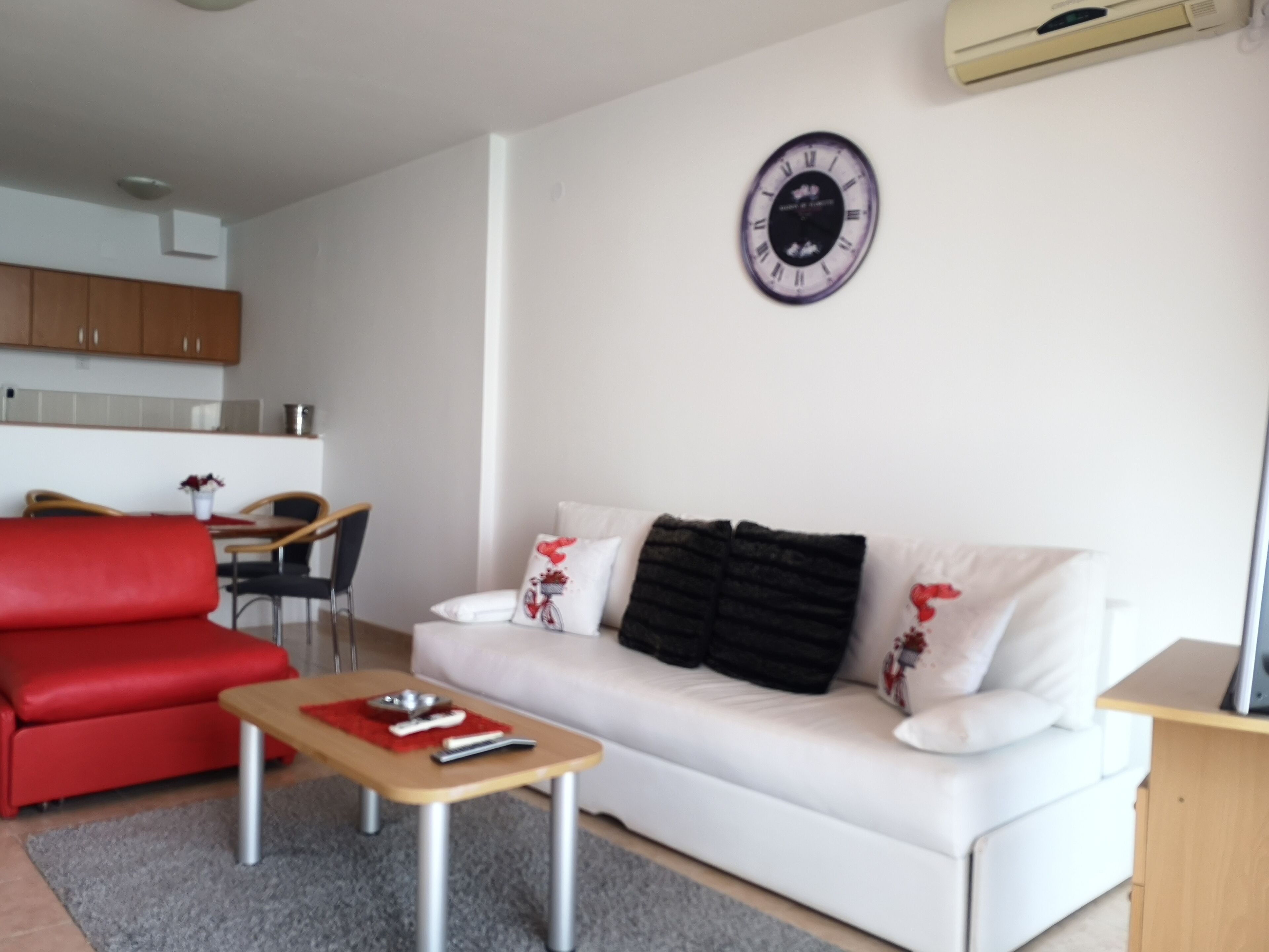 Una sala de estar moderna con un sofá rojo, un sofá blanco y una pequeña mesa de madera. Un reloj redondo está colgado en la pared sobre el sofá.
