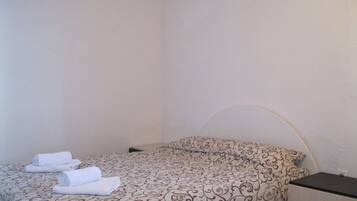 A single bed with a patterned bedspread and two rolled towels on it.