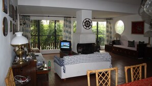 Een woonkamer met een televisie, een open haard, een bank en een eethoek met stoelen.