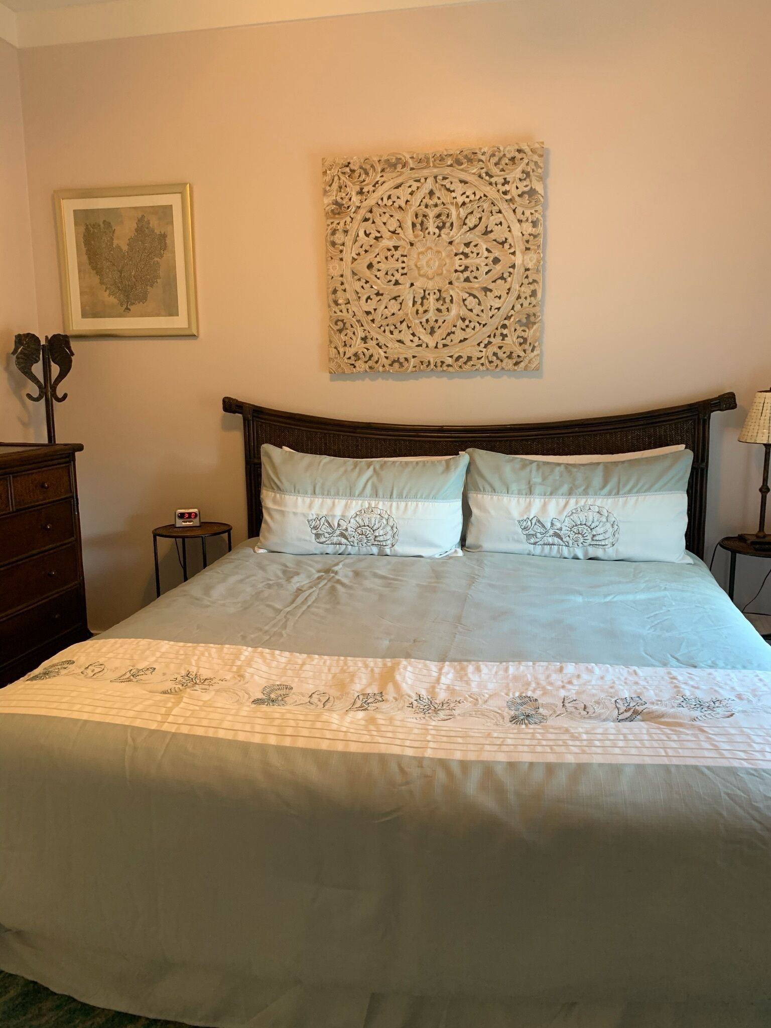 A neatly made bed with a floral bedspread and two pillows, a framed picture on the wall, and a decorative wall piece above the bed.