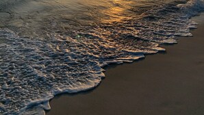 Une plage au coucher du soleil, avec des vagues qui viennent lécher le rivage.