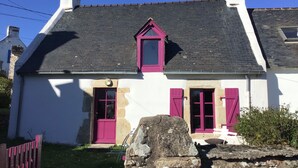 A white house with a dark roof, pink shutters, and a small triangular window.