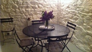 A round metal table with four chairs, a vase with purple flowers, and a stone wall background.