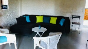 A black sofa with colorful cushions, a small round table, and wicker chairs in a room with a textured white wall.