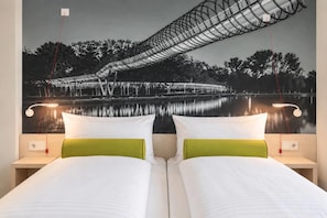 Un lit double avec une literie blanche et verte, deux tables de chevet avec des lampes, et une fresque murale représentant un pont au-dessus d’une étendue d’eau.