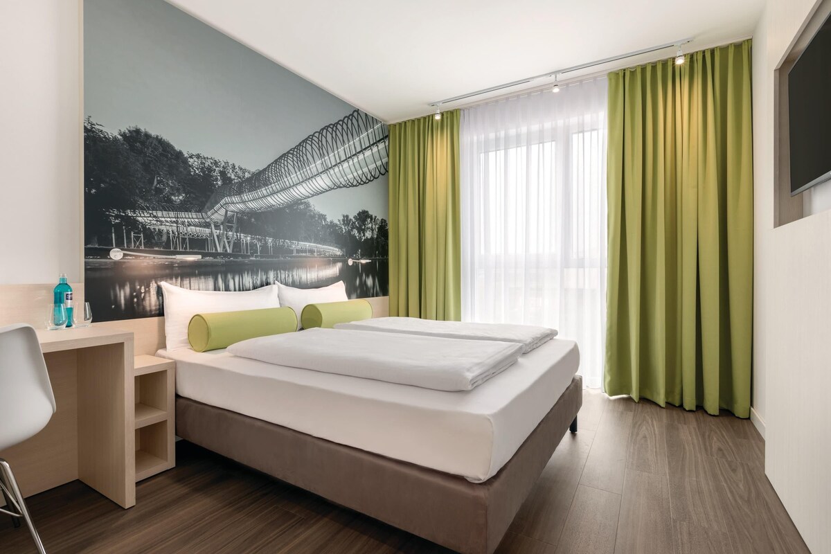 Een hotelkamer met een bed, een bureau, een stoel en een groot muurschildering.