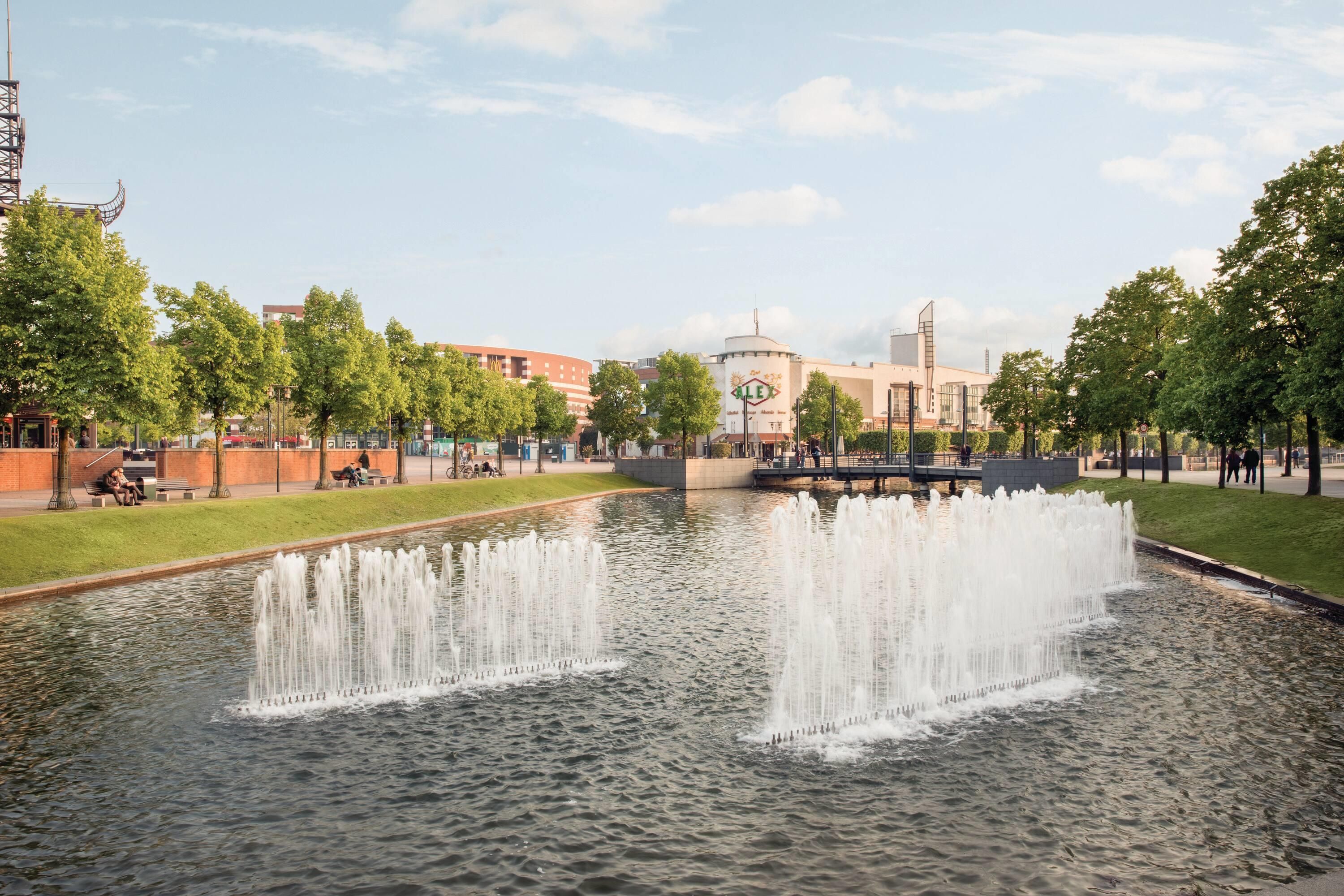 A public park with a fountain, benches, and a building with a sign in the background.
