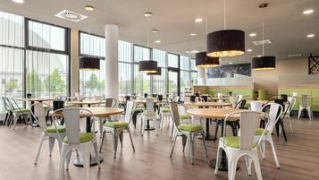 Una espaciosa cafetería con mesas y sillas redondas, ventanas amplias e iluminación colgante.