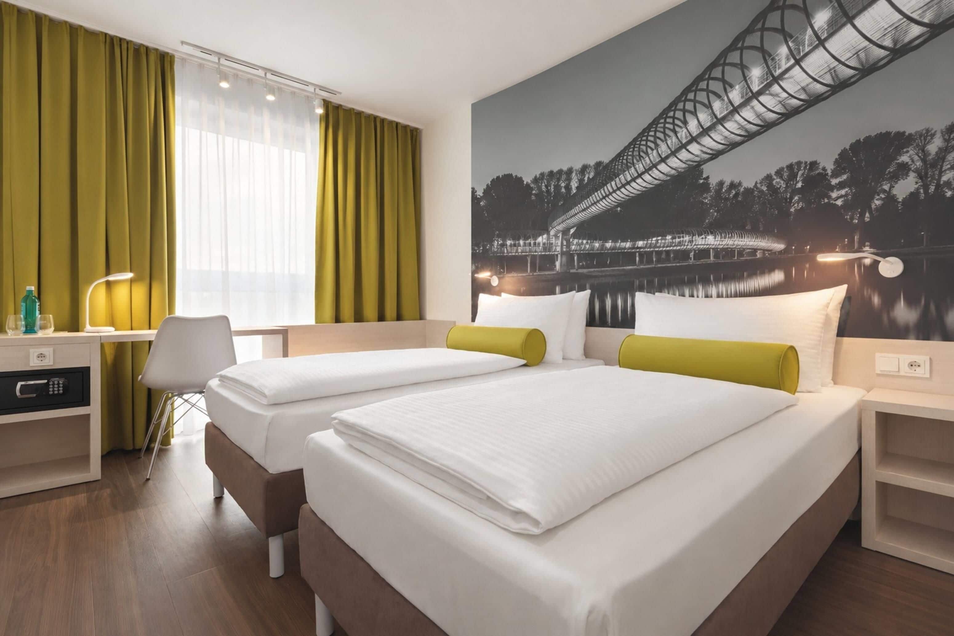 Een hotelkamer met twee bedden, een bureau, een stoel en een groot raam met gordijnen.