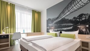 Een hotelkamer met twee bedden, een bureau, een stoel en een groot raam met gordijnen.