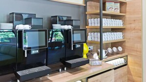 A coffee station with multiple espresso machines, a coffee display, and a shelf with mugs and a book. - Super 8 by Wyndham Oberhausen am Centro (Oberhausen)