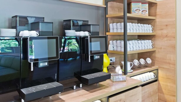 Een koffiehoek met meerdere espresso machines, een koffiepresentatie en een plank met mokken en een boek.