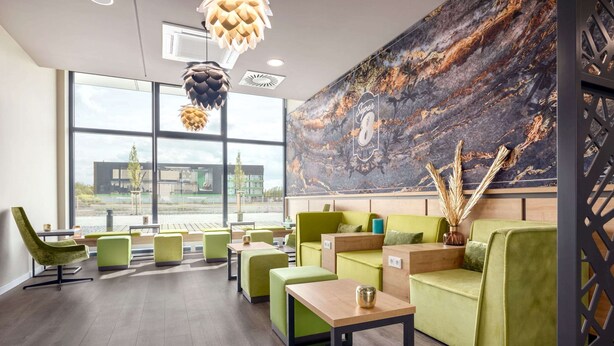 Een moderne lounge met groene zitplaatsen, grote ramen en een marmeren wand.