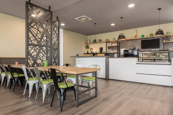 Un comedor moderno con una mesa y sillas de madera, una cocina con electrodomésticos y objetos decorativos en estanterías.
