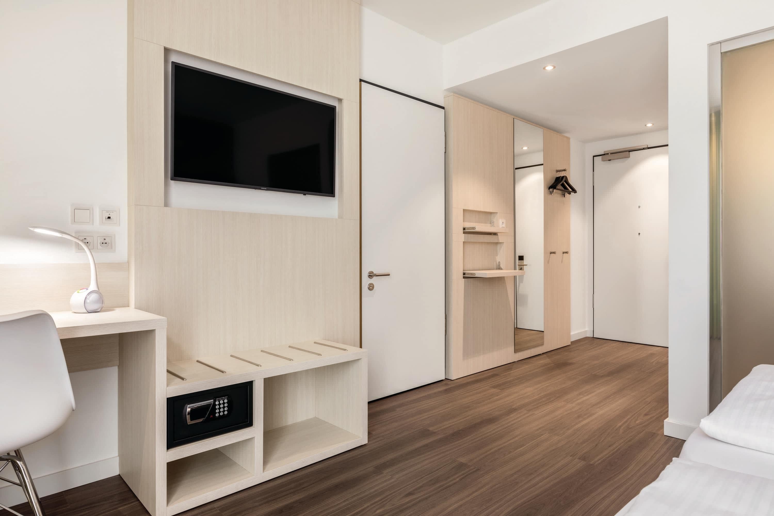 Habitació d'hotel moderna amb televisió de pantalla plana penjada a la paret, escriptori amb làmpada i microones integrada.