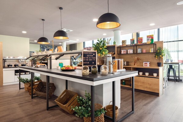 Un área de cocina moderna con una isla central, iluminación colgante y diversos productos alimenticios y utensilios de cocina exhibidos en estantes y la isla.