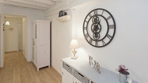 Ein Zimmer mit einem weißen Schrank, einer Wanduhr, einer Lampe und einem kleinen Regal mit Dekoration.