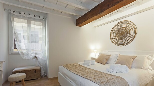 Ein Schlafzimmer mit einem großen Bett, einer hölzernen Bank, einer Wanddekoration und einem Fenster mit durchsichtigen Vorhängen.