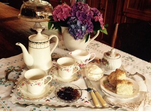 A table set with tea service, including a teapot, cups, saucers, a sugar bowl, a creamer, biscuits, and a floral arrangement.