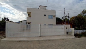 A modern two-story building with a gated entrance, a small porch, and a visible staircase leading to the entrance. - Residencial Malu (Penha)