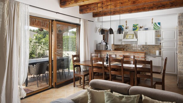 A dining area with a wooden table and chairs, a sofa, and a kitchen in the background. - Villa Paradis 6 - family villa with Pool (Butkovici)