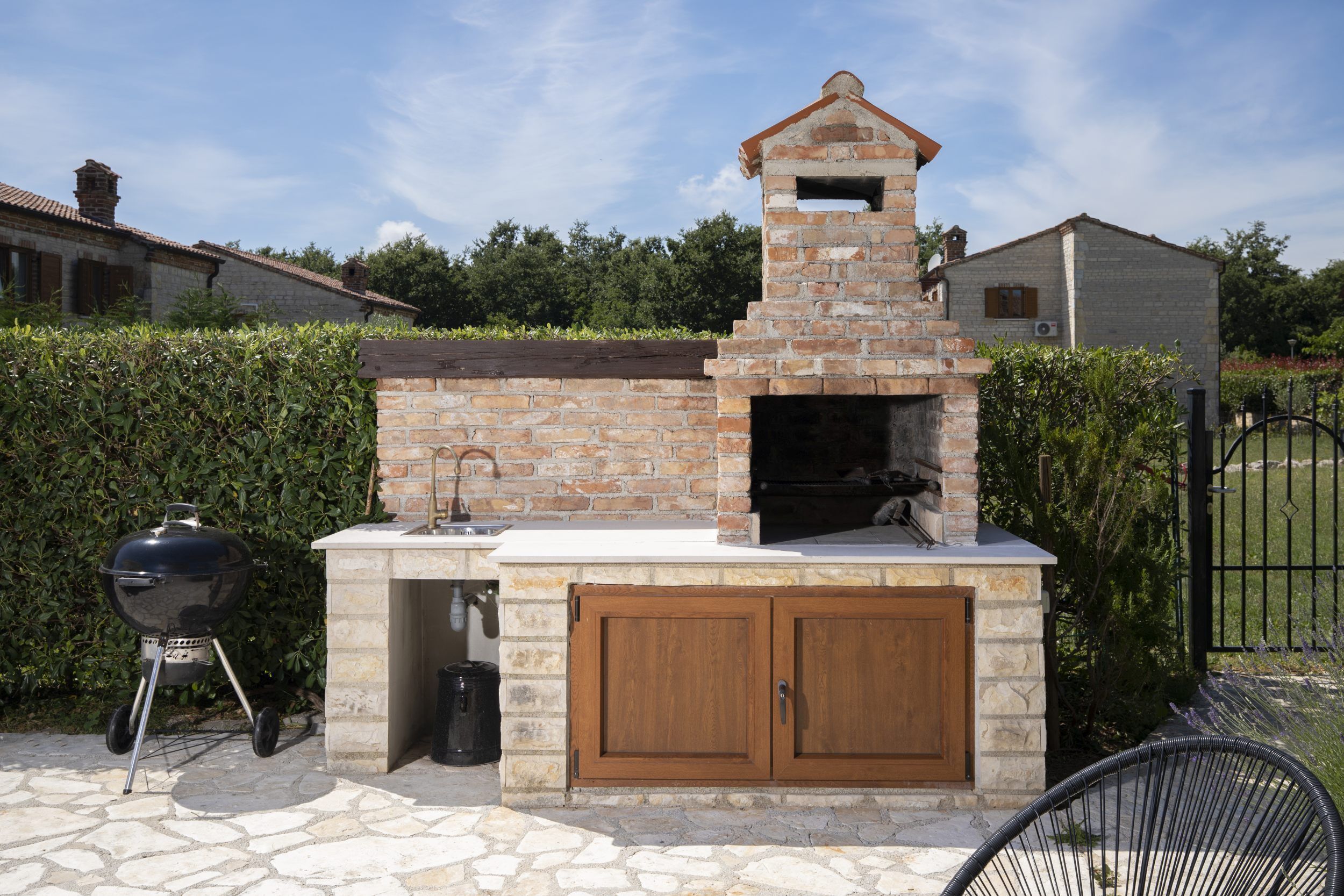 An outdoor brick oven with a chimney, a barbecue grill, and a stone patio.