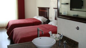 Habitación de hotel con dos camas, un espejo grande, un lavabo y un televisor.