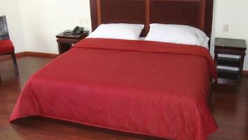 Un lit bien fait, avec une couvre-lit rouge, une tête de lit en bois et une table de chevet sur laquelle se trouve un téléphone.