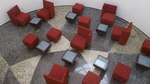 Un espacio circular con asientos de sillas rojas acolchadas y pequeñas mesas cuadradas.