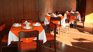 Un restaurante con paredes de madera y mesas dispuestas con manteles blancos y sillas naranjas.