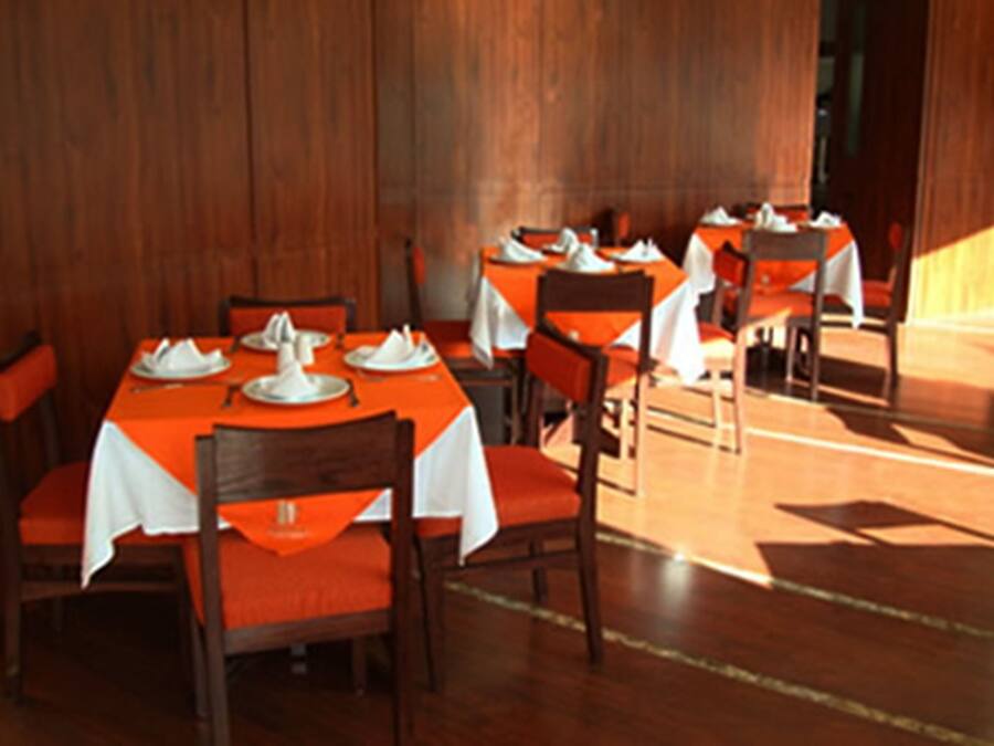 Un restaurante con paredes de madera y mesas dispuestas con manteles blancos y sillas naranjas.