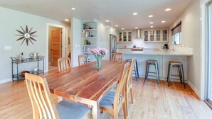Une cuisine moderne avec des meubles blancs, une table à manger en bois et un îlot central intégré avec des tabourets.