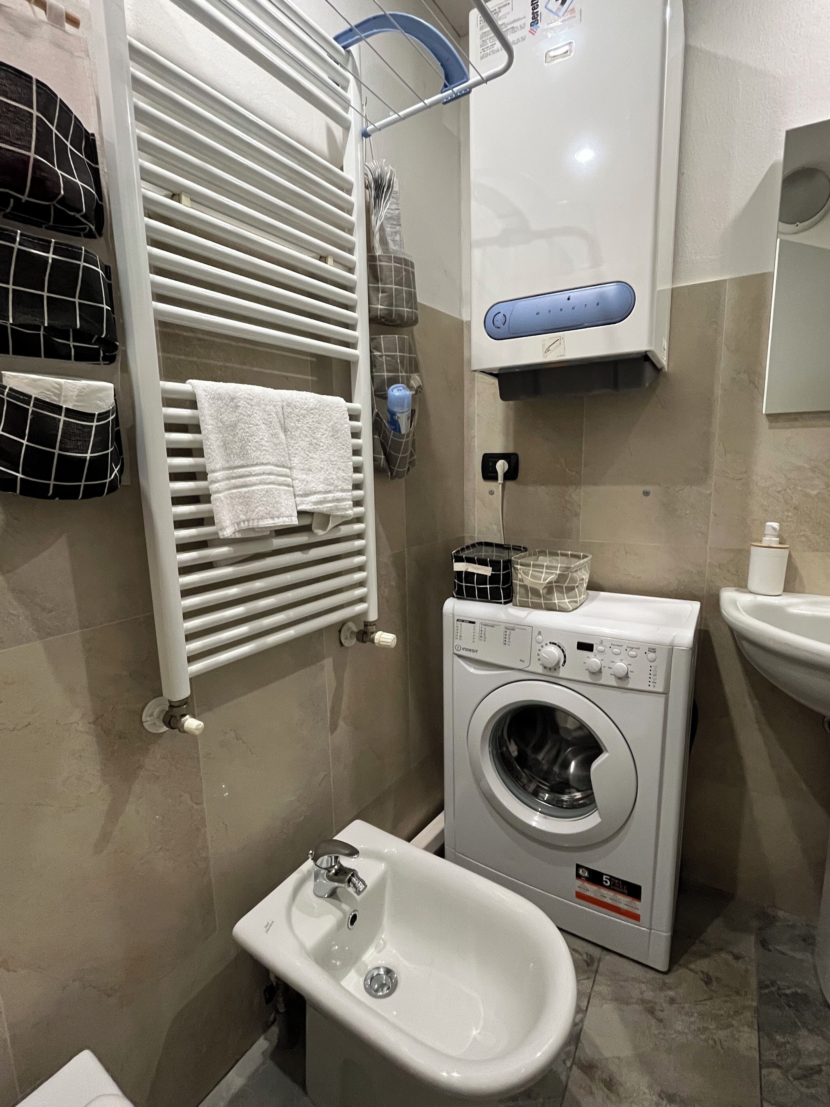 Ein Badezimmer mit weißem Handtuchhalter, einer Waschmaschine, einem Bidet und einem Waschbecken.