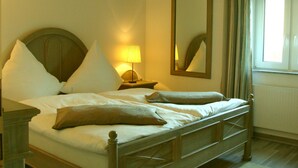 A neatly made bed with pillows, a bedside lamp, a mirror, and a window with curtains.