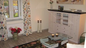A room with a glass coffee table, a white sofa, a cabinet with glass doors, a floral curtain, and a vase with flowers.