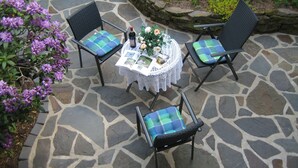 A stone patio with a round table and four chairs, each with a blue and green checkered cushion.