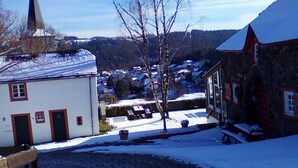 A cobblestone street in a snowy village with traditional buildings, a church steeple, and a clear blue sky.