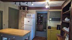 Eine kompakte Küche mit Holztisch, einem weißen Kühlschrank, einer Mikrowelle und einer Kaffeemaschine.