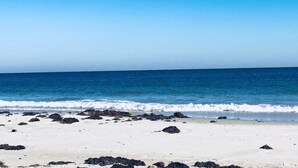 Een strand met helderblauw water en een zandstrand met verspreide rotsen.