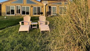 Een huis met een ruime veranda, twee Adirondack stoelen en een barbecue.