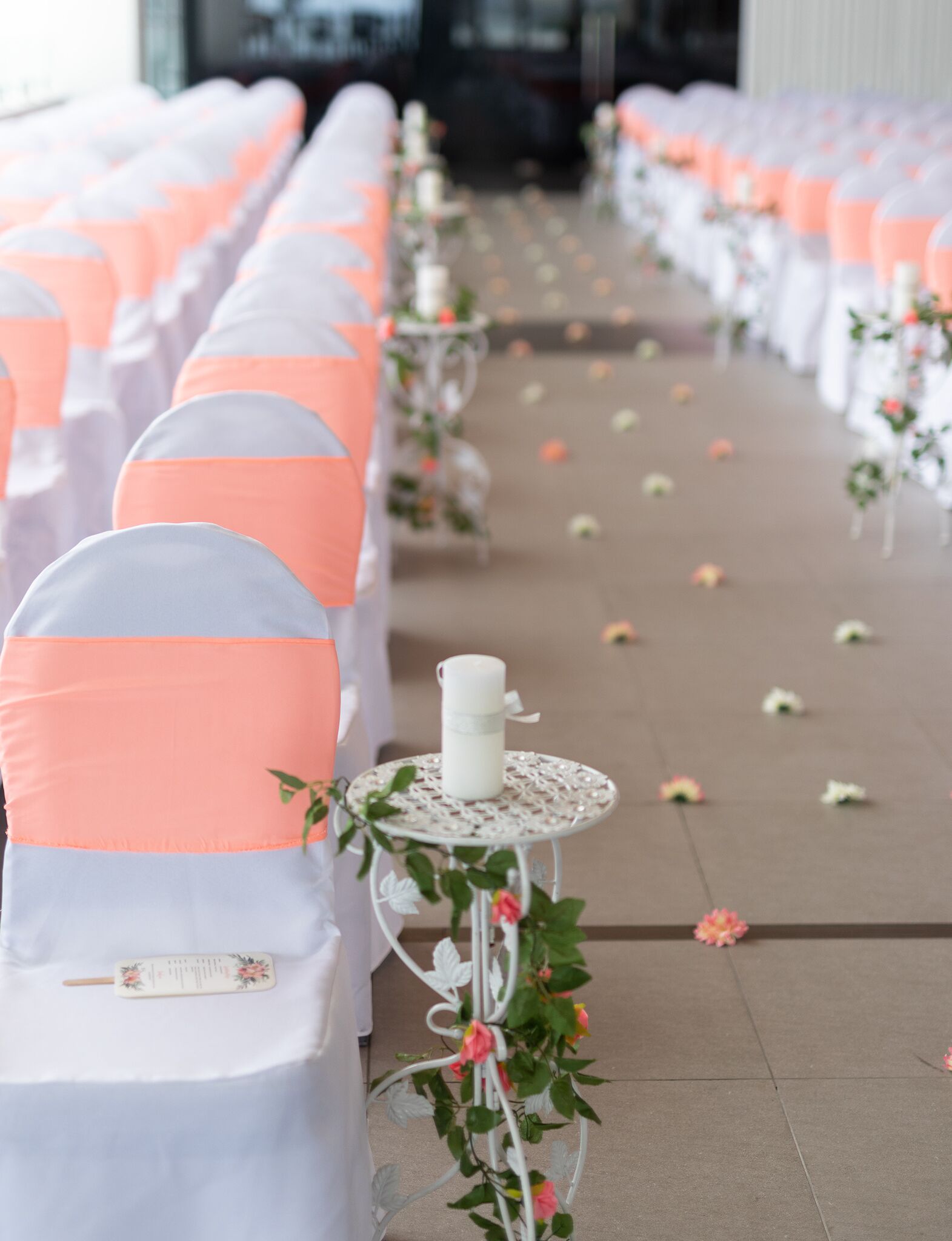 A row of chairs with white and peach-colored covers, arranged in a line with a white table and a candle between them.