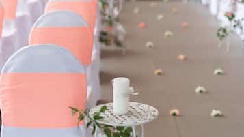 A row of chairs with white and peach-colored covers, arranged in a line with a white table and a candle between them.